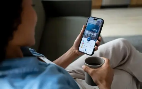 Kobieta sprawdza saldo konta na telefonie, trzymając kubek kawy.