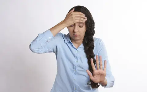 Kvinna med handen mot pannan, ser ut att ha ont i huvudet. Kanske gravid och känner sig illamående.