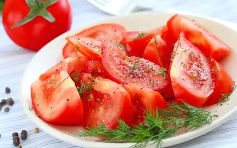 Une assiette de salade de tomates fraîches, assaisonnée de poivre noir et d'aneth. Un délice simple et coloré.