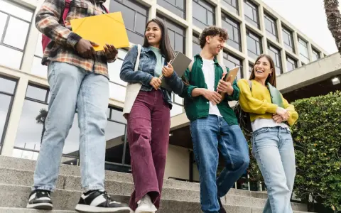 Studenci idą po schodach, rozmawiając i śmiejąc się. Czy ich wysoka średnia pozwoli im zdobyć stypendium?