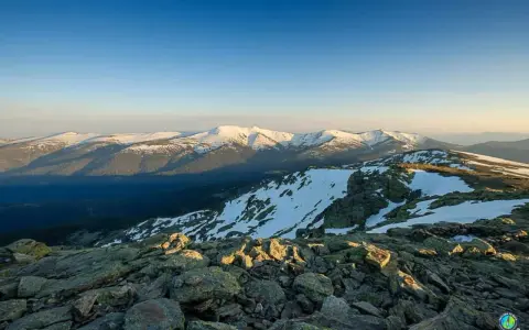 Paisaje montañoso nevado al amanecer, con rocas en primer plano y el pico Madrid en la distancia.