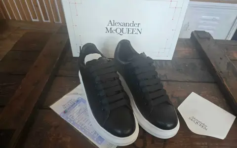 Czarne sneakersy Alexander McQueen na grubej, białej podeszwie, obok pudełka z logo marki.