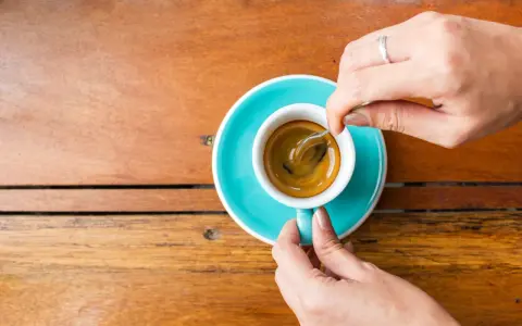 Mani che mescolano un caffè, nonostante si dica che il caffè è cancerogeno, il suo aroma attira.