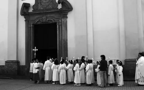 Dzieci w albach czekają przed kościołem, kiedy sa komunie. Trzymają świece, gotowe na uroczystość.