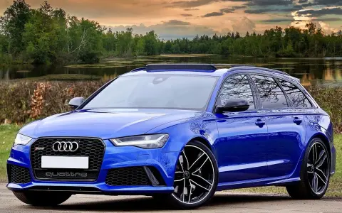 Niebieski **hatchback** z napędem quattro, zaparkowany nad jeziorem, z pięknym zachodem słońca w tle.