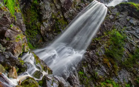 Vattenfall Storhogna forsar nerför en mossig klippvägg. Vattnet är silkeslent och omgivningen grönskande.