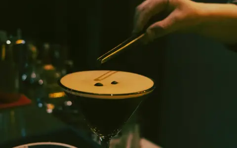 En hand lägger kaffebönor på en krämig espresso martini.