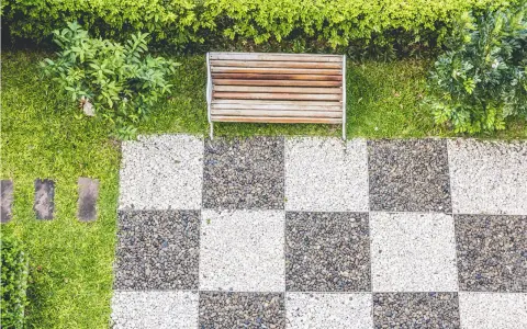 Ideas de suelo para terraza: un banco de madera sobre césped y un patrón de tablero de ajedrez de guijarros blancos y grises.