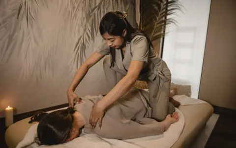 Relaksacyjny shiatsu masaż pleców. Terapeuta klęczy obok klienta leżącego na macie, wykonując delikatne naciski.