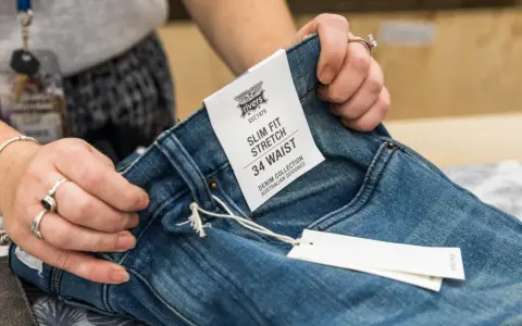 Dłonie trzymają dżinsy z metką "SLIM FIT STRETCH 34 WAIST". Czy to dobry rozmiar?