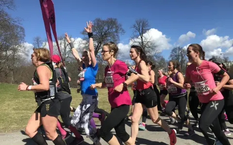 A group of women in running gear race on a sunny day, some with arms raised.