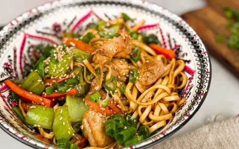 En skål med kycklingwok med nudlar, grönsaker och sesamfrön. En härlig och färgstark måltid.
