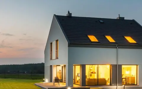 Une maison moderne et lumineuse, une maison autonome en France, avec de grandes fenêtres éclairées par une lumière chaude.