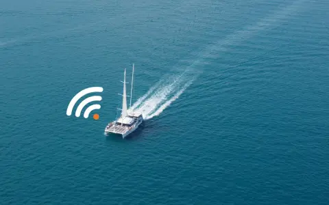 Un catamaran à voile navigue sur une mer bleue, avec un symbole de connexion Wi-Fi à proximité.