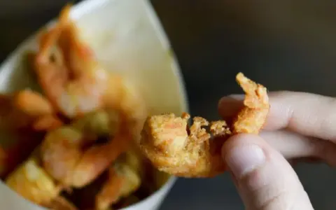 Una mano tiene un gambero croccante, parte di una deliziosa frittura di pesce servita in un cono di carta.