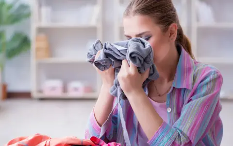 Kobieta wącha szare ubranie, szukając sposobu, jak pozbyć się zapachu stęchlizny z ubrań.
