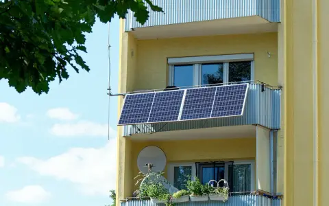 Två solceller monterade på en balkong på ett gult flerfamiljshus. Gröna växter i krukor på den nedre balkongen.