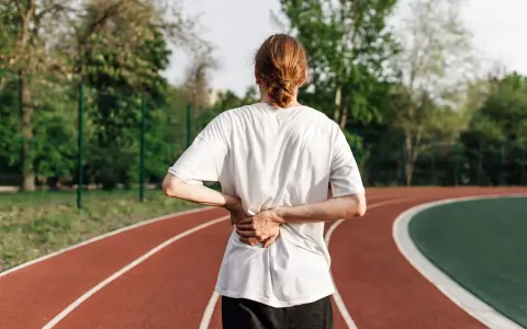 Une personne se tient sur une piste de course, le dos douloureux. La question se pose : peut-on courir avec une sciatique ?