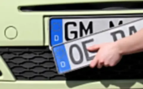 Dłoń trzyma niemieckie tablice rejestracyjne z literami "OE" i "GM".