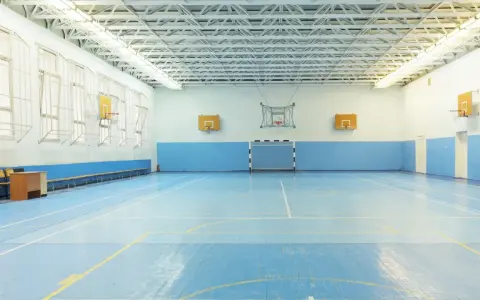 Pusta sala gimnastyczna z niebieską podłogą, boiskiem do koszykówki i piłki ręcznej. Idealne miejsce na zawody sportowe z doskonałym nagłośnieniem sali gimnastycznej.