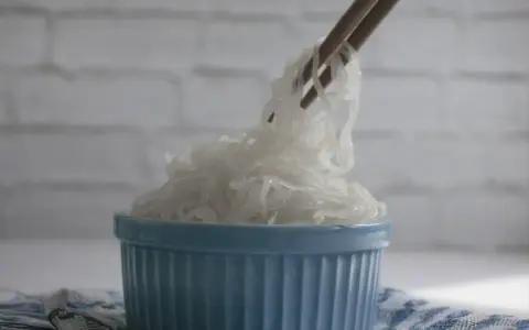 Patyczki podnoszą kłębek przezroczystego makaronu konjac z niebieskiej miseczki. To zdrowe danie, które warto wypróbować!