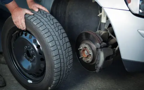 Mani che cambiano una gomma invernale, rispettando l'obbligo cambio gomme per la sicurezza stradale.