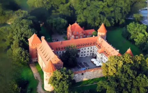Zamek w Bytowie otoczony zielenią, z czerwonymi dachami i kamiennymi murami, wygląda jak z bajki.
