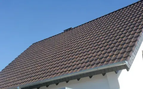 Dachówki ceramiczne na dachu domu, z widocznym okapem. Okap jest kluczowy, by wiedzieć, ile powinien wystawać dach poza ścianę, chroniąc ją przed deszczem.