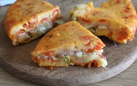 Fette di torta salata senza uova, ricca di pomodoro, formaggio filante e prosciutto, su un tagliere di legno.