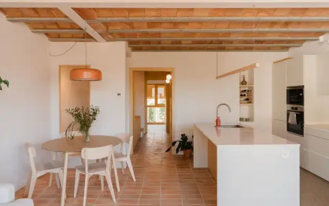 Comedor y cocina luminosos en una casa vieja decorada con poco dinero. Techos de vigas de madera y baldosas de terracota.
