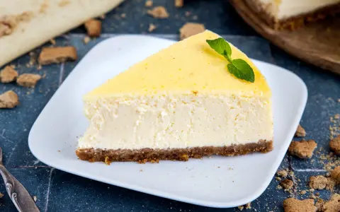 Ein cremiges Stück New York Cheesecake mit einem Keksboden, garniert mit Minze.