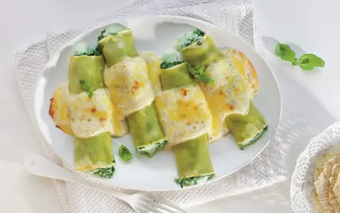 Pyszne cannelloni ze szpinakiem, zapieczone pod kremowym sosem serowym, ozdobione listkami bazylii.