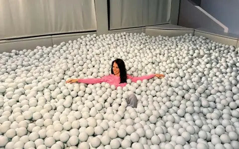 Mujer sonriente se sumerge en una piscina de bolas blancas, un divertido ikono madrid.
