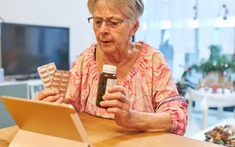 Starsza pani z tabletką w ręku sprawdza zwrot za leki dla seniorów.