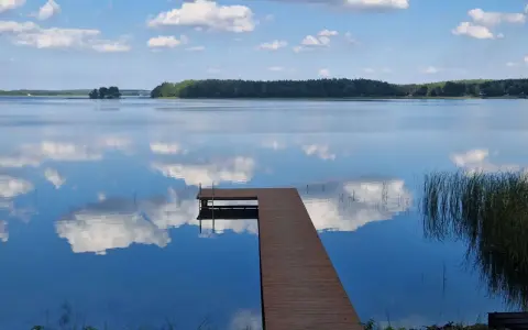 Drewniane molo na spokojnym jeziorze Wysockim, odbijającym błękitne niebo z białymi chmurami.