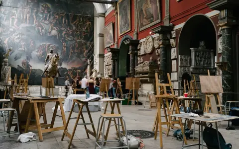 Des chevalets et des toiles dans une **école d'art appliqués**, devant une fresque monumentale et des sculptures. Des étudiants observent une œuvre.