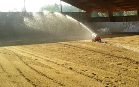 Arrosage d'une carrière équestre par un système mobile, créant un voile d'eau sur le sable.