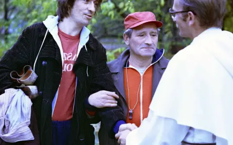 Czesław Nogacki w rozmowie z mężczyzną w białej szacie i z mężczyzną w czerwonej czapce.