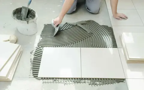 Układanie białej terakoty na kleju. Ręka z kielnią rozprowadza masę, tworząc idealną glazurę pod płytki.