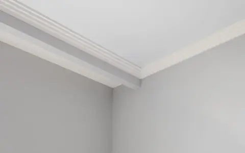 Angolo di una stanza con pareti grigie e soffitto bianco. Si nota uno stacco tra parete e soffitto con una modanatura decorativa.