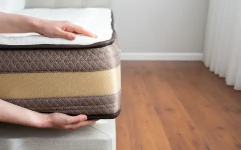 Mains posées sur un matelas, montrant sa bonne épaisseur. Le tissu matelassé marron et la bande beige suggèrent un confort optimal.