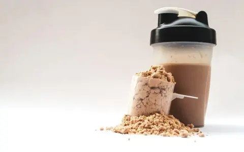 Ein Löffel Proteinpulver neben einem fertigen Proteinshake im Shaker. Perfekt für den proteinreichen Start in den Morgen.