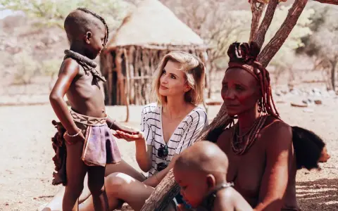 Ludzie Himba w Namibii: młoda kobieta rozmawia z dzieckiem i starszą kobietą w tradycyjnych strojach.