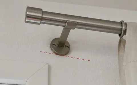 Eine Gardinenstange wird an der Wand befestigt, knapp unterhalb des Rolladenkastens. Die Halterung ist schräg montiert.