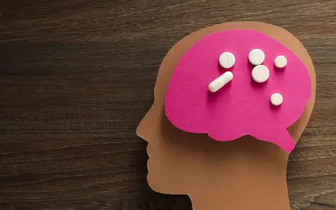 Papierowy profil głowy z różowym mózgiem, na którym leżą tabletki. Symbolizują one psychobiotyki na depresję, szukając ulgi dla umysłu.