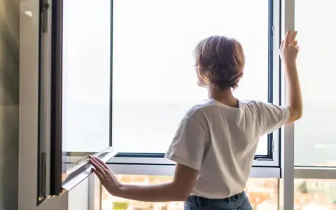 Frau stellt das Fenster ein, um frische Luft hereinzulassen.