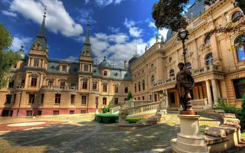 Pałac poznańskiego, z wieżyczkami i bogatymi zdobieniami, otoczony brukowanym dziedzińcem i zielenią.
