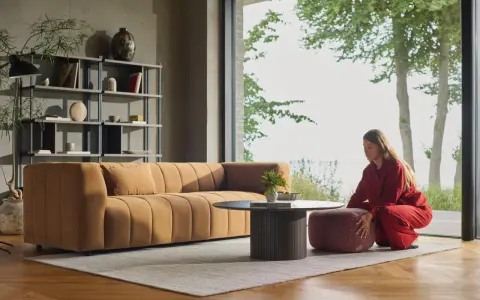 En kvinna i rött sitter på en pall bredvid en orange soffa. En dansk designer kan ha skapat detta stilrena vardagsrum.
