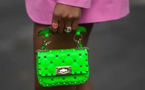 Borsa verde neon, colore complementare del fucsia, con borchie dorate e catena. Indossata da una mano con anelli.