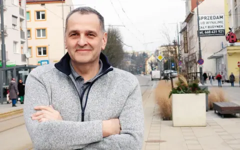 Sebastian Pieńkowski stoi na tle miejskiej ulicy z tramwajami i budynkami.